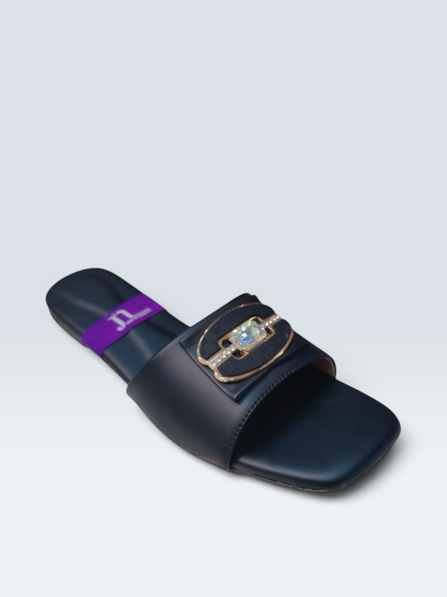 My Store 2 black flat slide sandals featuring a central crystal-inspired stone, gold-tone hardware, and monogram detail.