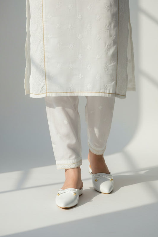 My Store 2 white patent leather-look pointed-toe mule sandals with a bow detail worn with white embroidered trousers.